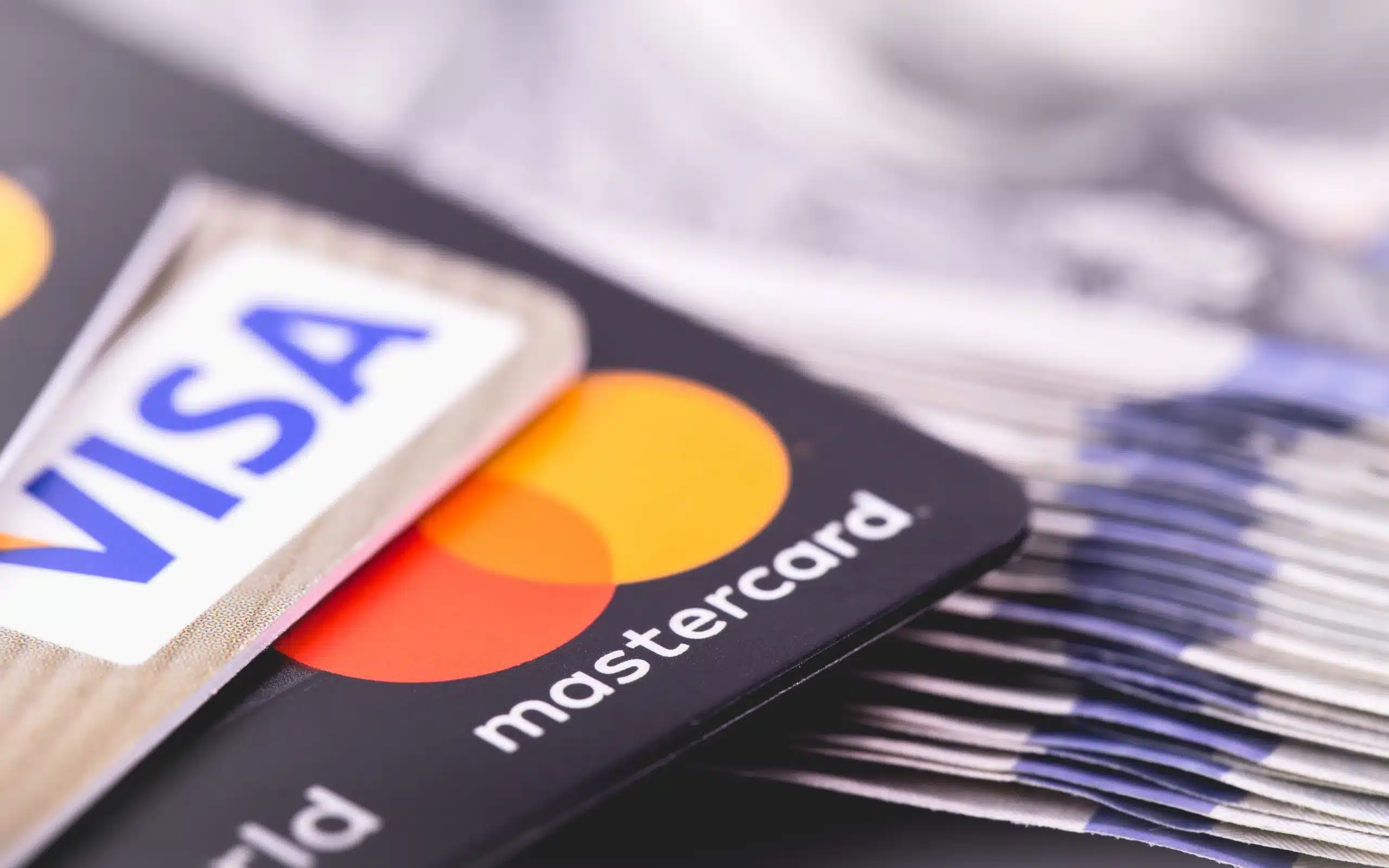 A Visa card and a Mastercard card resting on a fanned stack of US banknotes